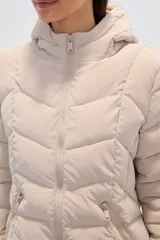Campera acolchada color beige claro, de largo medio, con capucha y cierre frontal. Presenta costuras horizontales y diagonales que crean un efecto matelassé.