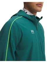 Campera de entrenamiento Under Armour Challenger, color verde esmeralda con detalles en amarillo neón. Presenta media cremallera frontal, capucha, bolsillo frontal con cierre y puños elásticos. Diseño técnico con tecnología repelente al agua y forro de malla.
