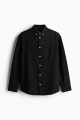 Camisa de algodón estilo Oxford, color negro, con cuello americano abotonado, bolsillo en el pecho y cierre frontal con botones blancos.