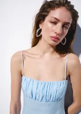 Vestido midi celeste de lino con escote recto, tirantes finos, cuerpo fruncido y falda evasé con volados.