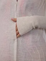 Saco largo de punto color blanco, confeccionado en 100% lana merino natural, con diseño jacquard de ramas, cuello alto, cierre frontal con pequeños botones y aberturas laterales.