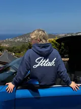 Hoodie azul marino con capucha y bolsillo frontal tipo canguro. Presenta un estampado gráfico en la espalda con la palabra 'Jttab' en tipografía cursiva blanca.