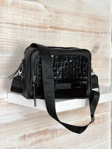Bandolera negra de cuero con textura tipo cocodrilo en la parte superior. Tiene correa de tela negra con letras blancas y herrajes plateados.