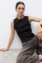 Top sin mangas color negro, con cuello redondo y detalle de ojalillos metálicos en los hombros. De corte ajustado y estilo minimalista.