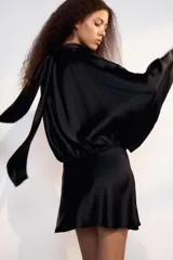 Vestido corto negro de tejido satinado, con cuello alto, mangas largas amplias y detalle de frunces en la cintura.