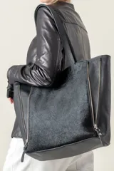 Bolso tipo tote de cuero negro con textura de pelo en el frente y cierres laterales.
