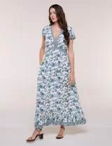Vestido maxi de rayón con estampado floral en tonos azules y marrones sobre base blanca, con escote en V, mangas cortas y falda larga fluida con volado en el ruedo.