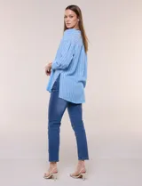 Blusa de silueta holgada a rayas verdes y blancas, confeccionada en tela liviana con textura arrugada. Presenta cuello en V profundo con botones frontales, mangas 3/4 de hombro caído y ruedo asimétrico con aberturas laterales.