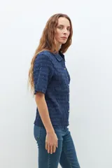 Camisa de manga corta en color bordó, confeccionada en tejido con textura de punto smock. Presenta cuello clásico, cierre frontal con botones y un ajuste entallado al cuerpo.