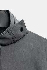 Cazadora gris con cuello subido, manga larga con trabillas y botón, bolsillos delanteros y cierre frontal con botones metálicos ocultos bajo sopata.