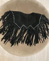 Chaleco corto de cuero azul marino, estilo western, con cuello solapa y profusión de flecos largos en todo el contorno. Presenta detalles de tachas metálicas plateadas a lo largo del borde del cuello y los hombros.