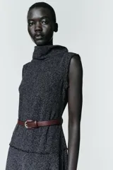 Vestido midi de tejido texturizado en color gris oscuro, con cuello alto fluido, diseño sin mangas y acabados deshilachados. Incluye un cinturón fino de cuero en color marrón con hebilla metálica y cierre de cremallera oculta en la espalda.