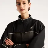 Campera New Balance Trackside de color gris oscuro, con cuello alto, cierre frontal completo y ribetes blancos en contraste. Cuenta con el logo de la marca bordado en el pecho.