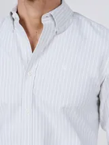 Camisa Oxford de corte regular fit, color blanco con finas rayas verticales, cuello buttondown y manga larga con puño simple. Cuenta con cierre frontal de botones y logo bordado en el pecho.