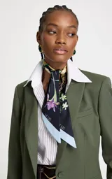 Pañuelo de forma rectangular con estampado floral sobre fondo azul oscuro y bordes en tono celeste claro, con el logo de la marca estampado en los extremos.