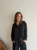 Camisa negra de crepe, con cuello camisero, mangas largas y cierre frontal con botones.