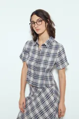 Camisa de manga corta con cuello camisero y botones frontales. Presenta un estampado de cuadros escoceses en tonos marrón oscuro y blanco/beige, con un calce entallado.