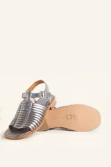 Sandalia plateada de cuero con tiras entretejidas, hebilla lateral y taco bajo.