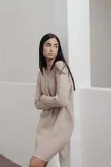 Vestido midi de tejido de punto fino en color beige, con escote en V y diseño de corte holgado. Presenta una textura acanalada y mangas largas.