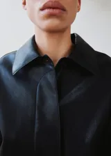 Chaqueta de cuero sintético negro con solapas clásicas, cierre frontal de botones ocultos y mangas largas amplias.