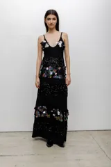 Vestido largo negro con escote en V y tirantes finos. Presenta un diseño de paneles horizontales que alternan bandas de lentejuelas negras brillantes con bandas decoradas con aplicaciones de lentejuelas iridiscentes en forma de pétalos.