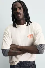 Camiseta de corte relajado color crudo, con cuello redondo y manga corta. Presenta un estampado gráfico pequeño en el pecho y un diseño grande en la espalda relacionado con el artista Post Malone.
