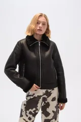 Campera corta negra de cuero sintético con cuello y puños de piel sintética negra, cierre frontal con cremallera y bolsillos laterales con cremallera.