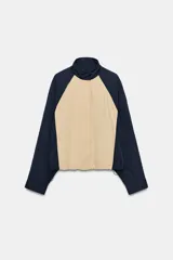 Cazadora combinada de nylon en color azul marino y beige, con cuello alto, cierre frontal oculto y bajo ajustable con cordón.