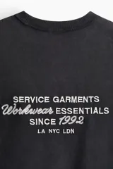 Remera de algodón de punto pesado en color negro con efecto lavado, cuello redondo acanalado, hombros caídos y pequeño estampado tipográfico en el pecho.