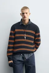 Jersey de punto con ajuste relajado, cuello redondo y manga larga. Presenta un diseño de rayas horizontales en color naranja sobre una base de color azul marino, con acabados en rib en puños, cuello y ruedo.