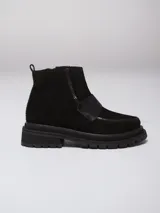 Botinetas de cuero y gamuza en tono marrón oscuro, con diseño de puntera reforzada y costuras decorativas en color rojo. Presentan una banda ancha sobre el empeine, cierre lateral y una lengüeta roja en el talón para facilitar el calce.