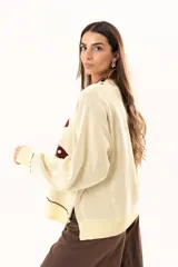 Buzo tejido de punto en color manteca, con diseño frontal de dos sardinas en color bordó. Presenta detalles bordados a mano en los bordes de las figuras y terminaciones con galón picot en cuello, puños y ruedo. Posee un corte holgado y aberturas laterales en el bajo.