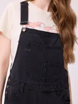 Mono de jean negro con diseño de jardinera, de corte recto y holgado, con bolsillos frontales y laterales.