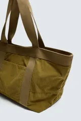 Bolso tipo shopper de gran capacidad, confeccionado en tejido con textura de pana. Cuenta con dos asas de mano resistentes, un bolsillo frontal plano y cierre principal mediante botón a presión. El interior incluye un bolsillo con cierre de cremallera.