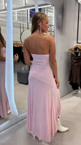 Vestido largo rosado con brillo, strapless y diseño asimétrico con volados en la parte inferior.