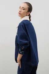 Campera de jean azul oscuro con cuello de pana en color crema. Presenta cierre frontal metálico, bolsillo con cierre en el pecho y bolsillos laterales. Diseño de corte holgado con mangas largas.