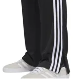 Pantalón negro de Adidas, modelo Firebird, con tres rayas blancas a los costados y logo bordado en el muslo.