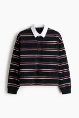 Remera manga larga de punto de algodón con diseño a rayas horizontales en negro, bordó y blanco. Presenta cuello estilo polo en color blanco, cierre frontal parcial con botones ocultos y puños acanalados.