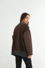 Saco tipo cardigan de punto gris con diseño bicolor, mangas largas acolchadas negras y bolsillos frontales también acolchados en color negro. Presenta cierre frontal con botones y terminaciones en tejido acanalado.