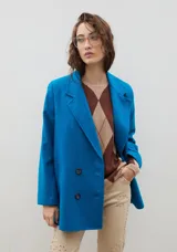 Blazer de lana con diseño bicolor, cuerpo en color negro y mangas en color crema. Presenta un corte holgado, cierre cruzado con doble botonadura y solapas amplias en contraste.