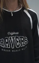 Sweater de punto negro con cuello redondo, mangas largas con franjas laterales blancas y puños en punto rib. Presenta un diseño gráfico bordado en el pecho con la inscripción 'RAVERS' y detalles en blanco.