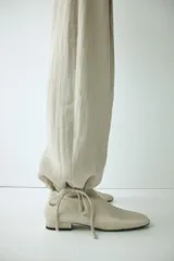 Pantalón tobillero de tiro alto en tejido arrugado color beige, con cierre de botón, bolsillos laterales y bajo ajustable con cordón.
