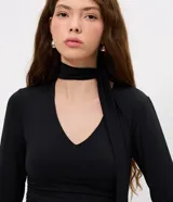 Blusa entallada de microfibra color blanco, con escote en V, mangas largas y detalle de frunces en los laterales. Presenta un lazo integrado en el cuello que permite anudarlo, aportando un toque sofisticado al diseño.
