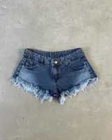 Short de denim azul con efecto desgastado, tiro medio y botamanga con flecos deshilachados.