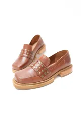 Mocasín de cuero color suela con punta cuadrada y detalle de tachas metálicas en la faja frontal. Cuenta con suela de caucho con vira a la vista.
