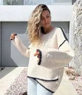 Sweater de punto en color crudo con detalles de costuras y bordes en color negro. Presenta un diseño de corte holgado, cuello redondo y mangas largas con puños acanalados.