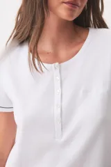 Camisón blanco de algodón, con mangas cortas, escote redondo y cierre frontal parcial con botones. Presenta ribetes oscuros en los puños.