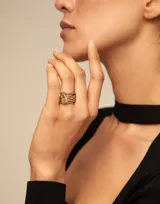 Anillo múltiple bañado en oro, compuesto por varias bandas apiladas con un dije colgante en forma de candado grabado con el logo de UNO de 50.