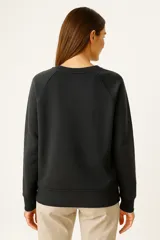 Sudadera negra de cuello redondo, manga larga tipo raglán y corte holgado.