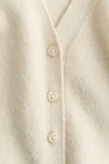 Saco de punto suave con lana, color beige, escote en V, botonadura frontal y ribetes acanalados en puños y dobladillo.